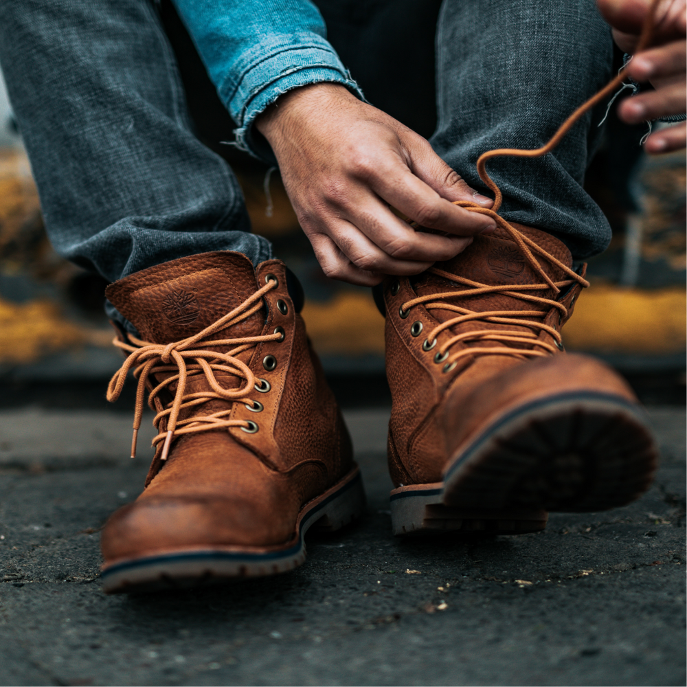 Man with tan brogues tied to his rucksack walking past a store on the street